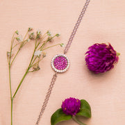 A sterling silver bracelet with a round pink gemstone charm, displayed on a neutral background with floral accents.